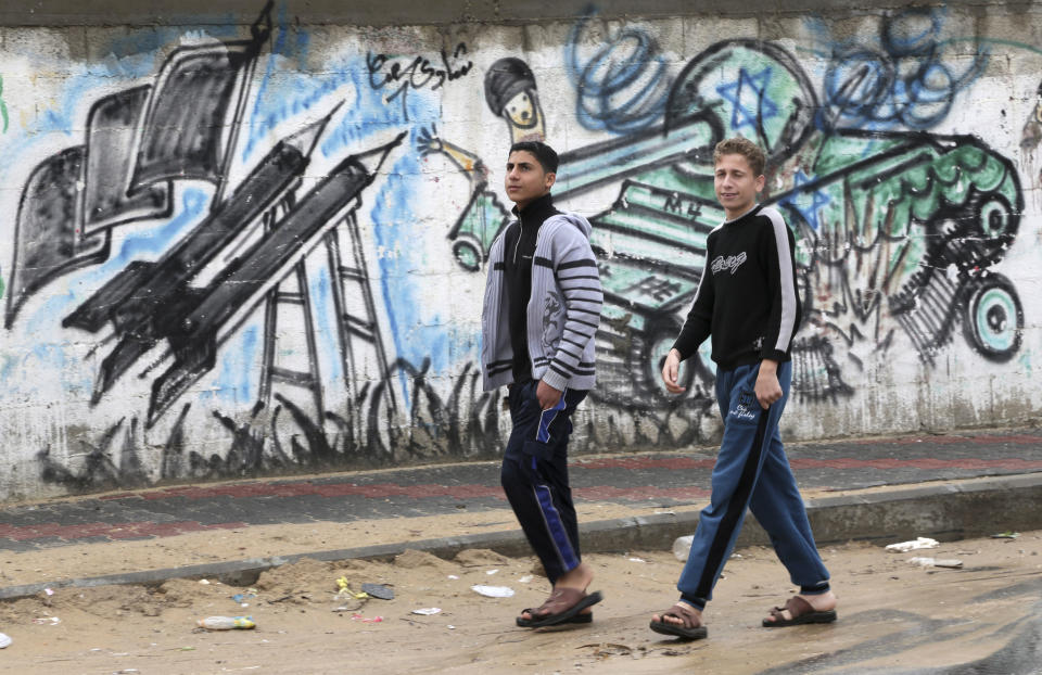 Palestinians walk past graffiti of rockets and an exploded Israeli tank in Gaza City, in the northern Gaza Strip, Thursday, March 13, 2014. Gaza militants resumed their rocket fire toward Israel on Thursday, striking the outskirts of two major cities a day after launching the largest barrage since an eight-day Israeli offensive in late 2012. Gaza militant groups said they resumed their rocket fire in response to what they say are Israeli "provocations" and violations of a cease-fire, including an airstrike that killed three Islamic Jihad militants earlier this week. (AP Photo/Adel Hana)