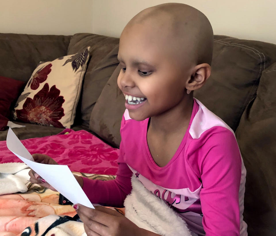 In this April 1, 2020 photo provided by The Valerie Fun, cancer patient Sophie Chhowalla, 8, reads an uplifting note from stranger Sarah Schneider while resting at her home in Berkeley, N.J. Schneider began writing encouraging emails and sharing riddles with children undergoing treatment for dire illnesses after people and organizations began quarantining due to the coronavirus pandemic. "I wanted them to know they're not alone," said Schneider. (Courtesy of The Valerie Fund via AP)