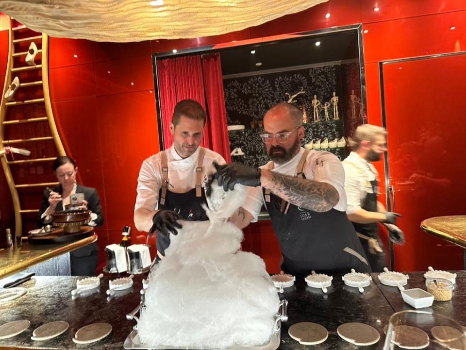 Two men in aprons with gloves on pouring white ice-like substance onto a pile