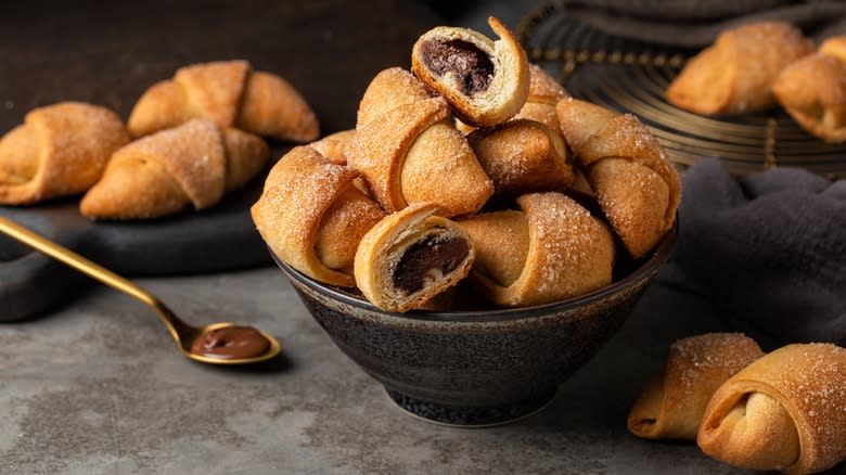A bowl of rugelach cookies next to a spoon of chocolate
