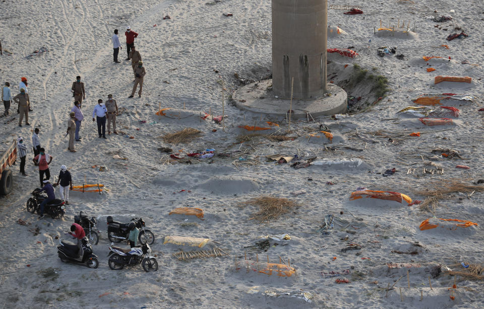 Policemen stand next to the bodies buried in shallow graves on the banks of Ganges river in Prayagraj, India, Saturday, May 15, 2021. Police are reaching out to villagers in northern India to investigate the recovery of bodies buried in shallow sand graves or washing up on the Ganges River banks, prompting speculation on social media that they were the remains of COVID-19 victims. (AP Photo/Rajesh Kumar Singh)