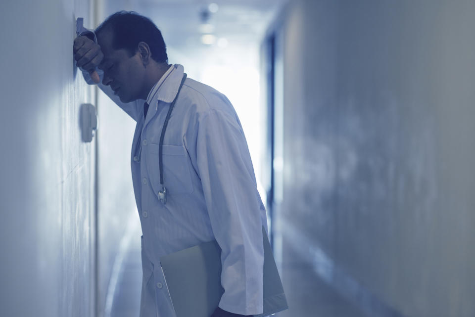 Upset male doctor standing at corridor and leaning against the wall