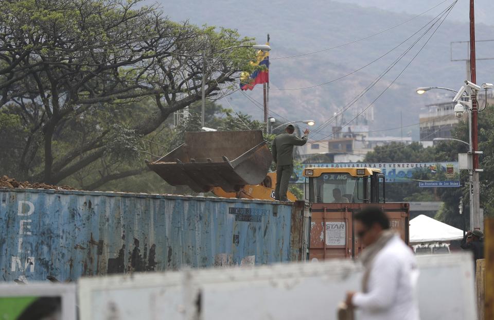 A Venezuelan soldier gives directions to a front end loader as it fills with dirt one of the containers that blocks the Venezuelan side of the Simon Bolivar International Bridge in La Parada, Colombia, on the border with Venezuela, Thursday, Feb. 28, 2019. The border between Colombia and Venezuela has been closed indefinitely by the Venezuelan government. (AP Photo/Martin Mejia)