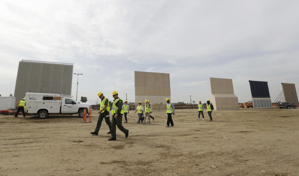 File - In this Oct. 19, 2017 file photo, people pass border wall prototypes as they stand near the border with Tijuana, Mexico, in San Diego. Montana's Senate president is proposing the state give more than $8 million to help build President Donald Trump's proposed wall on the Mexican border. Scott Sales, a Republican, says his proposal is a "small token" to show border security "is of vital interest to all citizens regardless of what state they live in." (AP Photo/Gregory Bull, File)