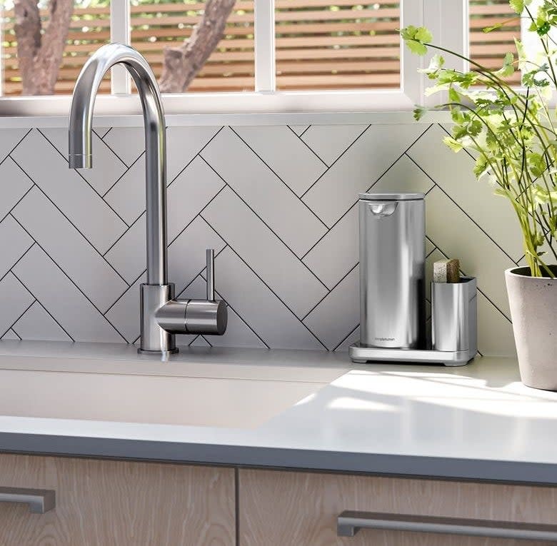 the silver soap dispenser and caddy next to a sink