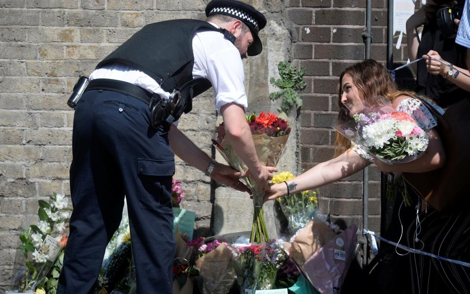 A police officer helps a woman leave flowers near the scene  - Credit: HANNAH MCKAY/REUTERS