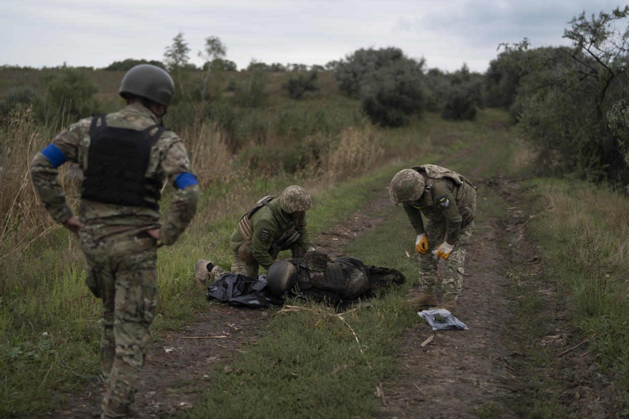 Ukrainian servicemen examine the body of a Ukrainian soldier in a retaken area near the border with Russia in Kharkiv region, Ukraine, Saturday, Sept. 17, 2022. (AP Photo/Leo Correa)