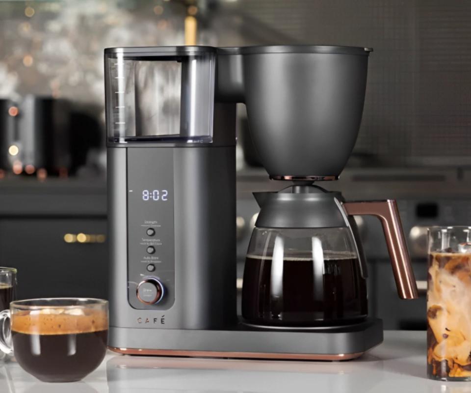 A drip coffee maker on a kitchen counter beside a full coffee cup