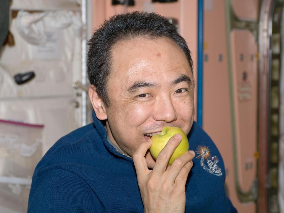 astronaut Satoshi Furukawa smiling eats a fresh apple on the space station
