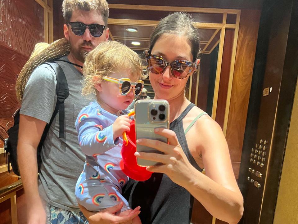 A woman taking an elevator selfie holding her baby with a man next to them.