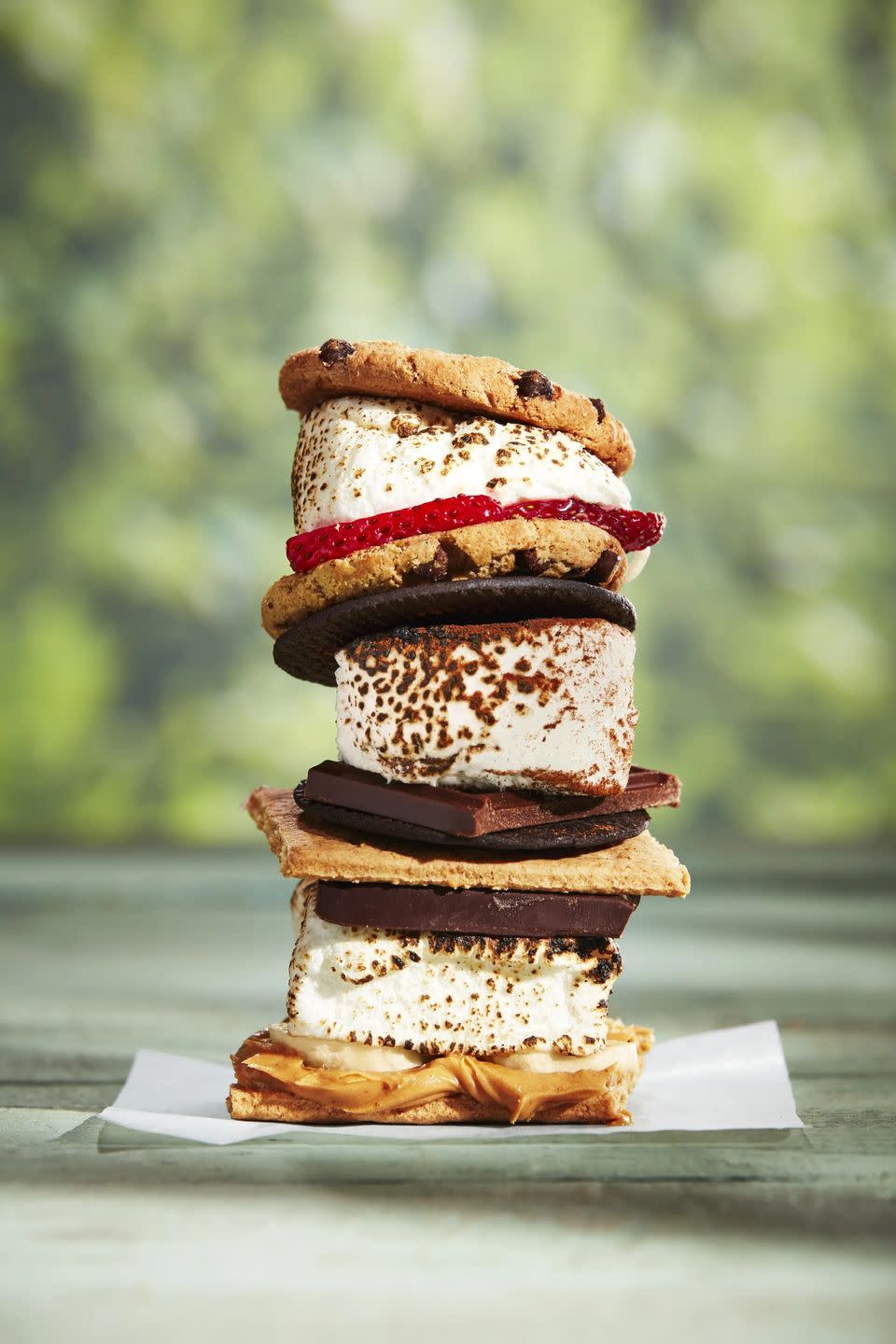 3 smores sandwiches stacked vertically one with peanut butter and banana one with strawberries on a chocolate chip cookie and another on chocolate cookies