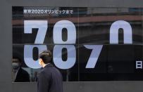 A passersby, wearing a face mask due to the outbreak of the coronavirus disease (COVID-19), walks past a screen counting down the days to the Tokyo 2020 Olympic Games