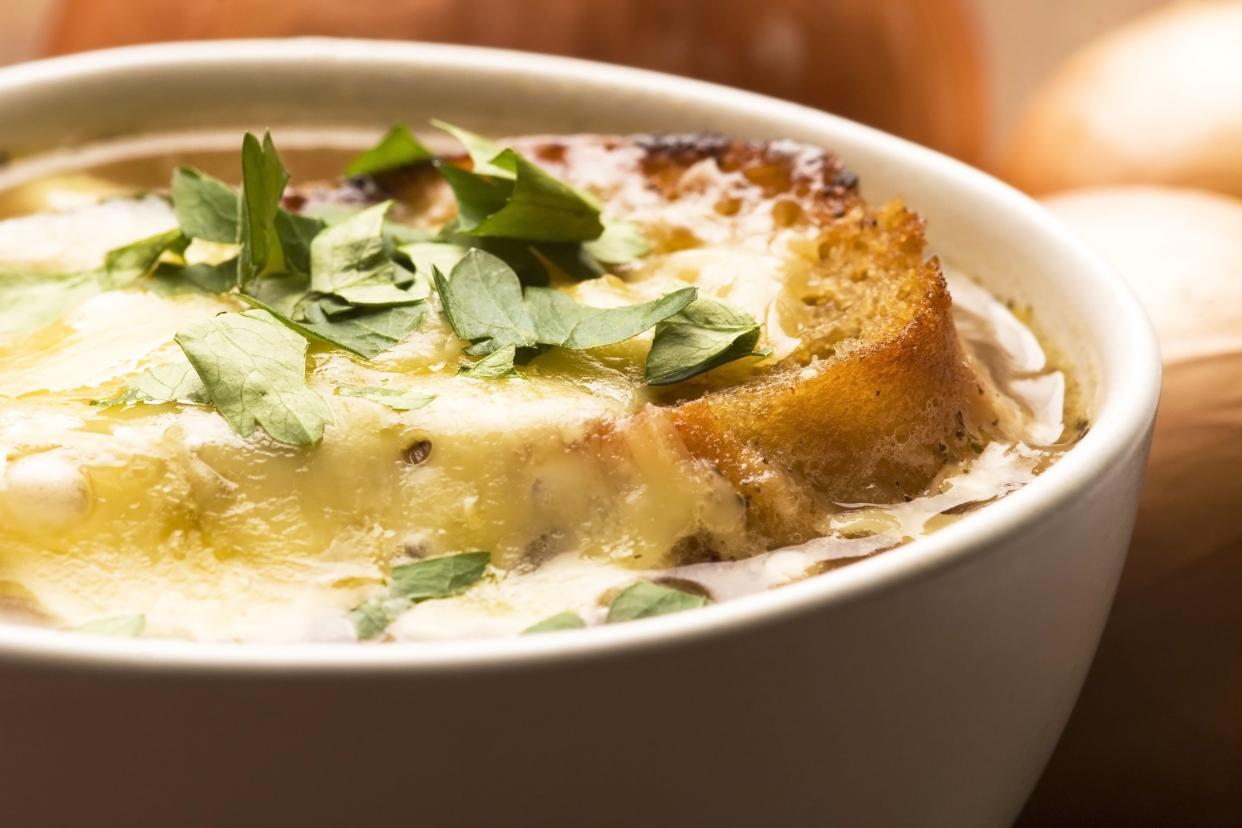 Closeup of French onion soup in a white porcelain bowl, vertical, on a blurred background of ingredients