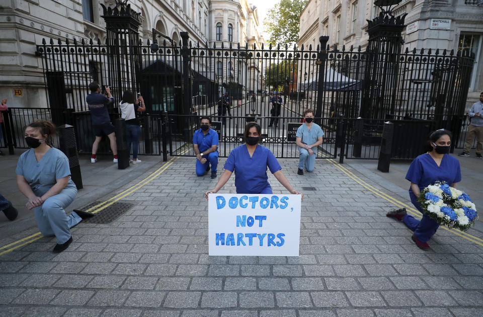 Doctors and nurses kneel in front of Downing Street ahead of the clap to remember colleagues who have died fighting the coronavirus pandemic in London, Thursday, May 28, 2020. (AP Photo/Frank Augstein)