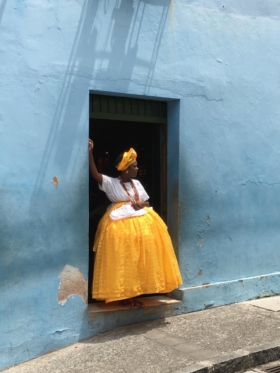 First Place<br />"Baiana in yellow and blue"<br />The picture was taken in Salvador de Bahia, Brazil, spontaneously, after a truck drove by. The woman with traditional clothes of a &ldquo;baiana&rdquo; was looking after the truck, during her work break.<br />Shot on iPhone 6S.