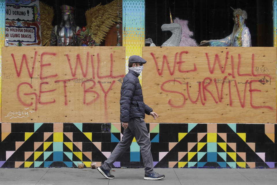 FILE - In this Saturday, April 18, 2020 file photo, a man wears a face mask while walking past signs posted over windows of a store in the Haight-Ashbury district in San Francisco. (AP Photo/Jeff Chiu)