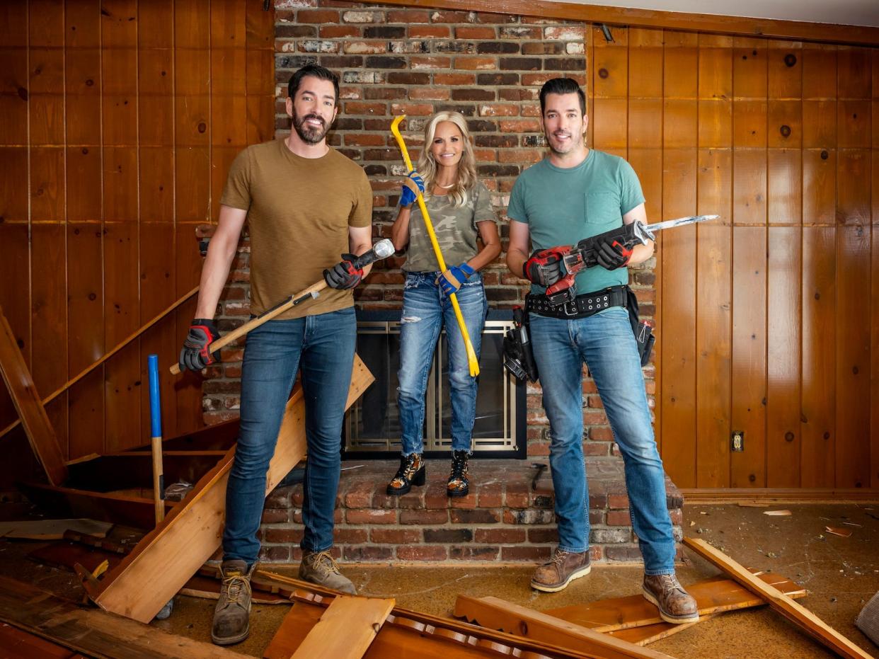 Kristin Chenoweth and the Property Brothers pose holding tools in front of a fireplace.
