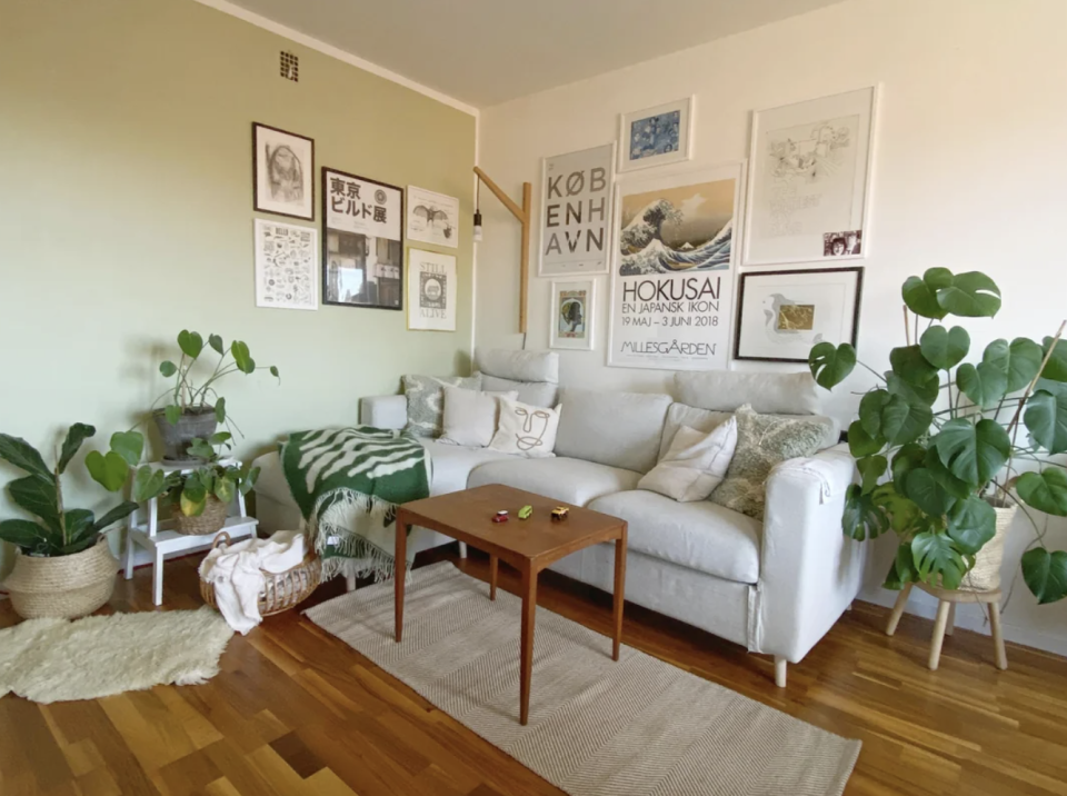 A cozy living room corner in Stockholm, Sweden, featuring a beige sofa adorned with cushions, a small wooden table, and green plants. Wall art is displayed above the sofa