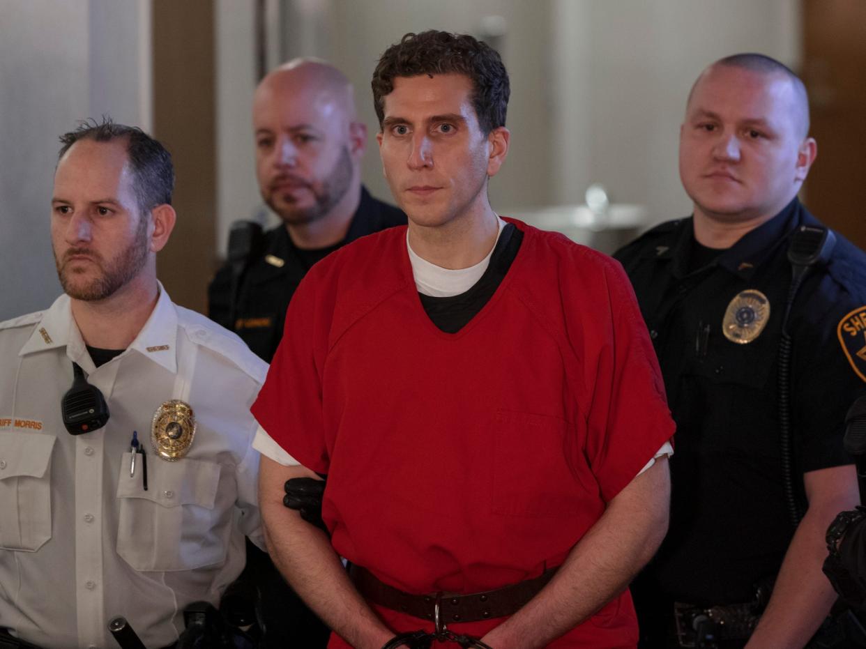 A man in an orange jumpsuit in the center is surrounded by three police officers