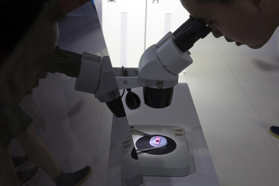 FILE - A visitor to the 21st China Beijing International High-tech Expo looks at a computer chip through the microscope displayed by the state-controlled Tsinghua Unigroup project which has emerged as a national champion for Beijing's semiconductor ambitions in Beijing, China on May 17, 2018. Chips are a top priority in the ruling Communist Party's marathon campaign to end China's reliance on technology from the United States, Japan and other suppliers Beijing sees as potential economic and strategic rivals. If it succeeds, business and political leaders warn that might slow down innovation, disrupt global trade and make the world poorer. (AP Photo/Ng Han Guan, File)
