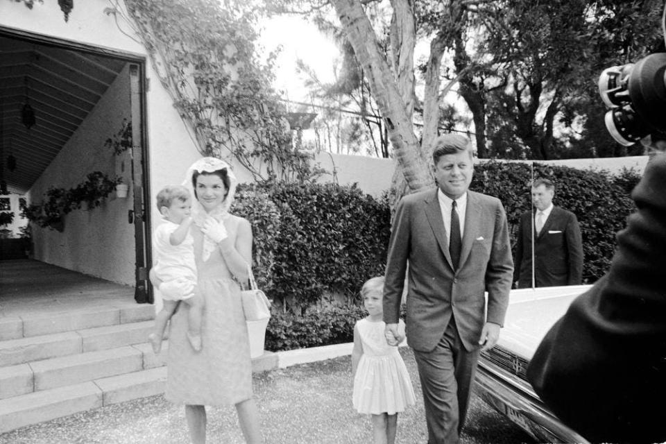 President John F. Kennedy and family depart a private chapel at the residence of Ambassador Joseph P. Kennedy Sr., in Palm Beach, Florida, following an Easter Sunday service. Kennedy holds Caroline Kennedy's hand; first lady Jacqueline Kennedy carries John F. Kennedy, Jr.; Secret Service agent stands at right (behind car).