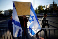 <p>An Israeli man holds a picture depicting the peace symbol of dove with an olive branch next to Israeli flags as a border policeman secures the area near the entrance to Mount Herzl cemetery ahead of the funeral of former Israeli President Shimon Peres in Jerusalem on Sept. 30, 2016. (REUTERS/Amir Cohen)</p>