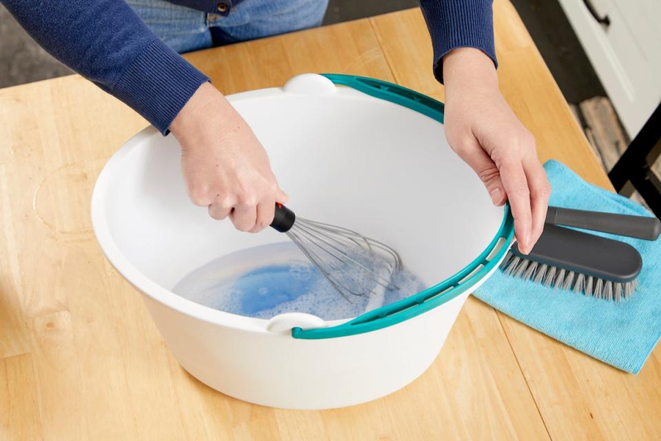 Woman whisking liquid upholstery cleaner in a bucket.