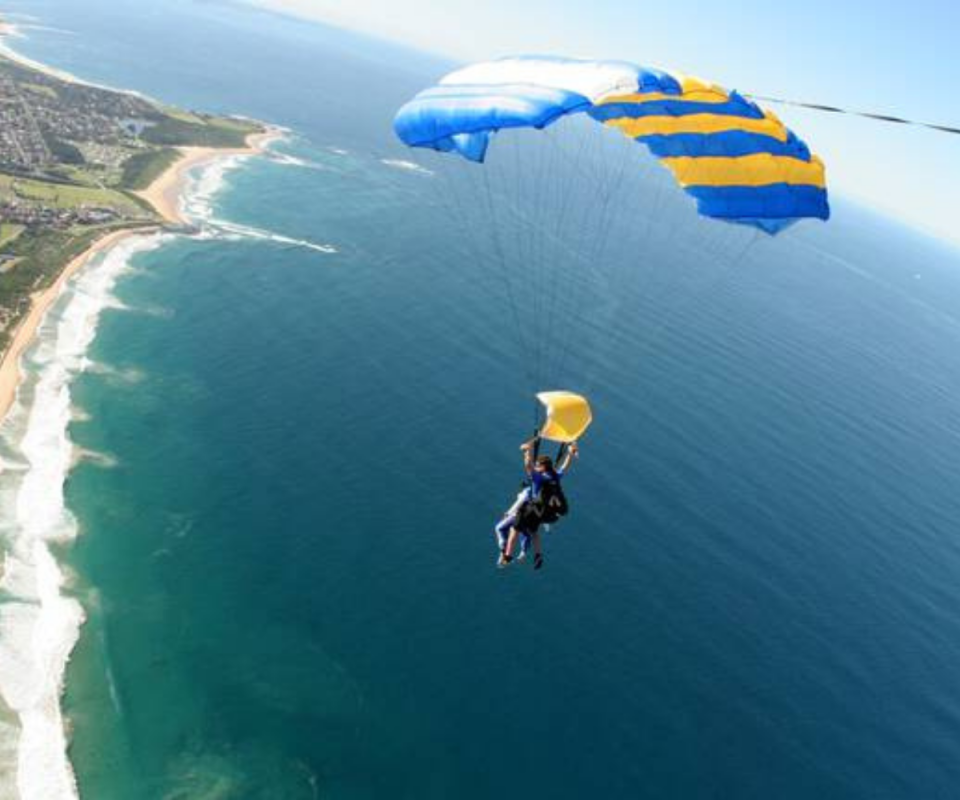 A person is skydiving above an ocean with a blue and yellow parachute.