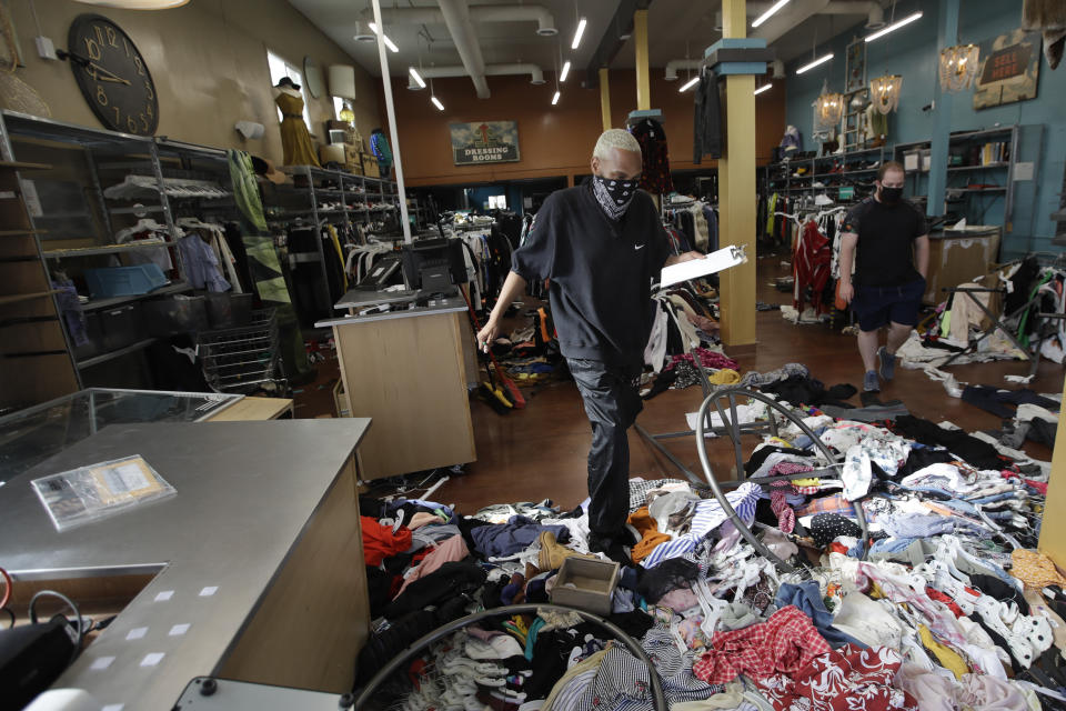 Terrel Ransom, center, store manager for Buffalo Exchange walks over clothes in the damaged store, Sunday, May 31, 2020, in Los Angeles, following a night of unrest and protests over the death of George Floyd, a black man who was in police custody in Minneapolis. Floyd died after being restrained by Minneapolis police officers on May 25. (AP Photo/Marcio Jose Sanchez)