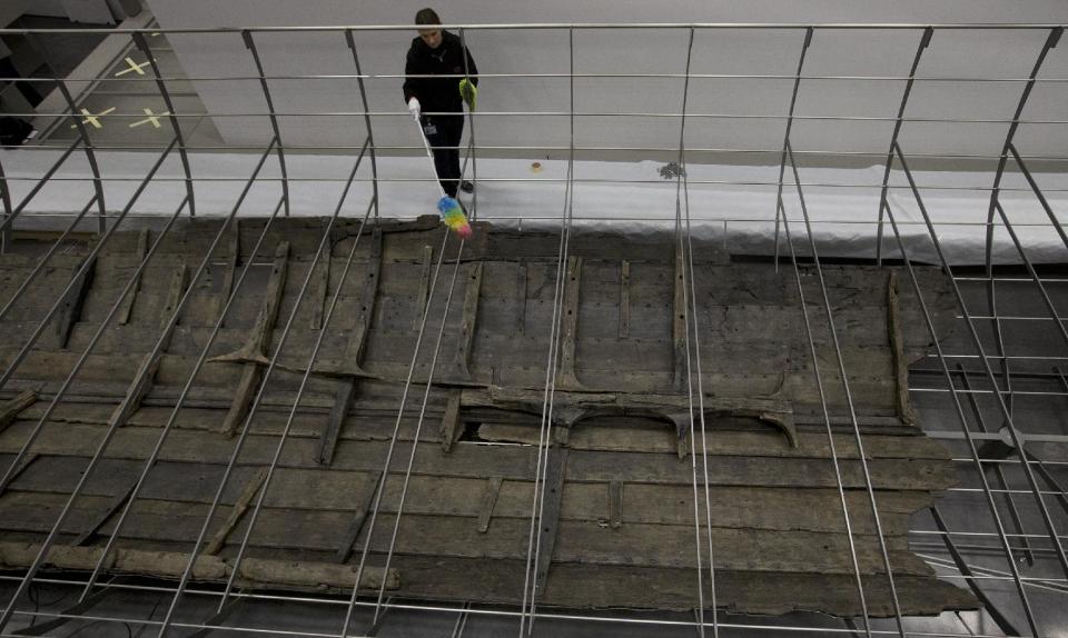 A conservator uses a feather duster to clean part of the modern metal skeleton above the wooden planks of the Viking ship known as Roskilde 6, of which only about 20 per cent of the timber remains and is dated to around 1025 AD, at the British Museum in London, Friday, Jan. 17, 2014. The ship was excavated from the banks of Roskilde Fjord, Denmark in 1997. It will be part of a Viking exhibition at the museum that will open to the public on March. 6, 2014. (AP Photo/Alastair Grant)