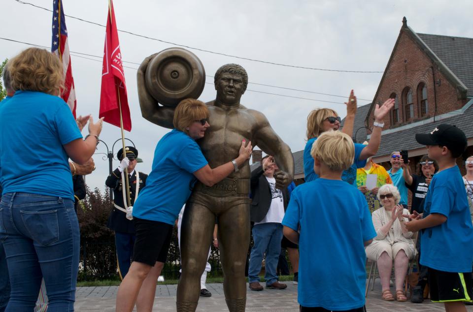 Sherri Brozoski, daughter of Reggie "Da Crusher" Lisowski, hugs the life-sized bronze statue of her father at Crusherfest in South Milwaukee.