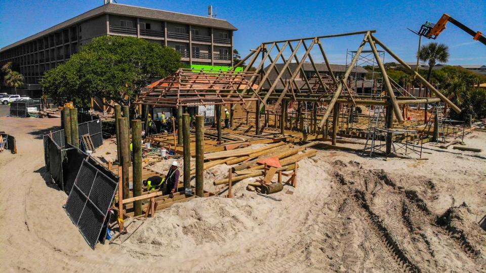 Workers, bottom left, work on the Tiki Hut’s new musical stage as a mechanical lift, upper right, holds a beam of the hut itself as seen on Tuesday, April 9, 2024, at the Beach House Hilton Head Island.