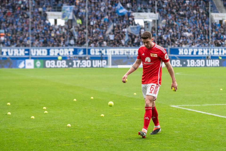 Nationalspieler Robin Gosens von Union Berlin sammelt beim Auswärtsspiel bei der TSG Hoffenheim Tennisbälle ein, die Fans zum Protest auf den Rasen geworfen haben.  - Copyright: picture alliance / Eibner-Pressefoto | Eibner-Pressefoto/Wolfgang Frank