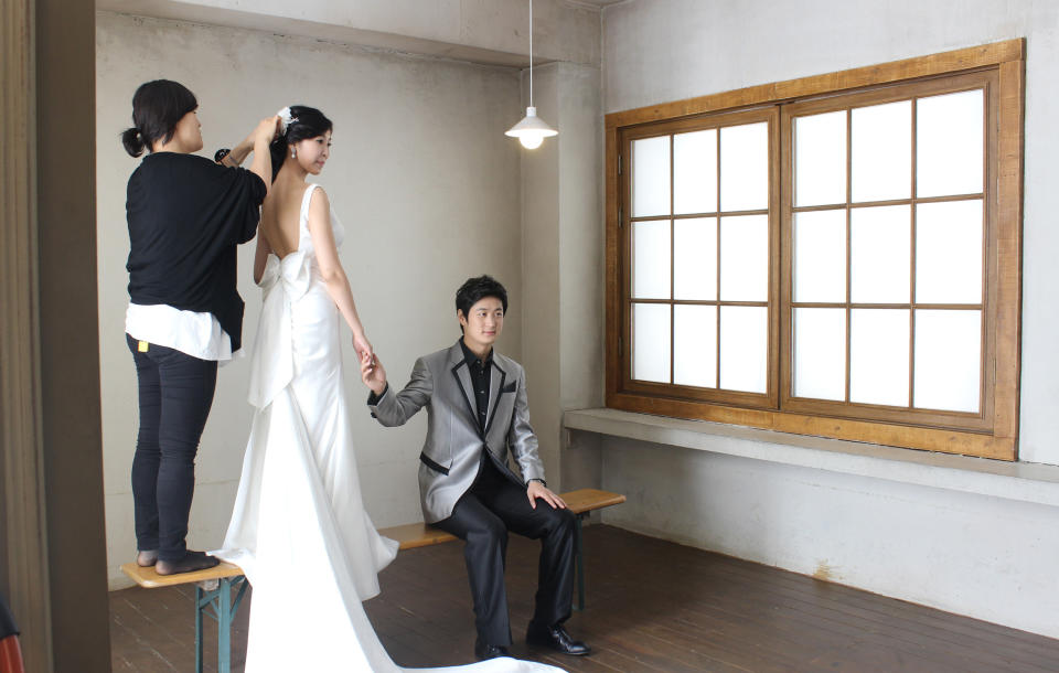 Chen Jingjing, right, and Yang Candi of Beijing, China, look for cues from their South Korean photographer as an assistant fixes Yang’s hair ornament during an eight-hour wedding shoot Tuesday, July 30, 2013, at a wedding studio in southern Seoul, South Korea. China is the source of one quarter of all tourists to South Korea, and a handful of companies in South Korea’s $15 billion wedding industry are wooing an image-conscious slice of the Chinese jet set happy to drop several thousand dollars on a wedding album with a South Korean touch. (AP Photo/Elizabeth Shim)