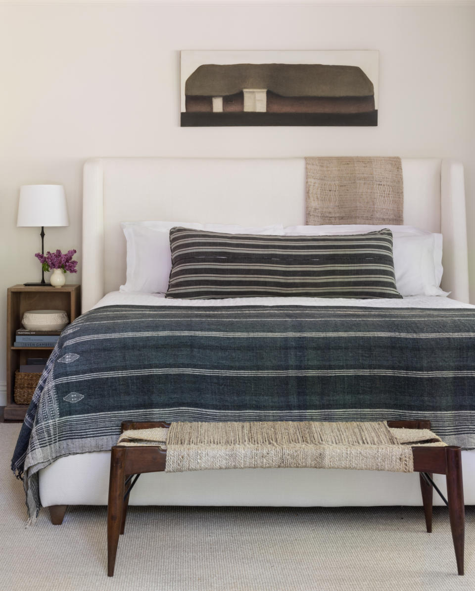 Off-white upholstered bed with striped blue throw and wooden bench