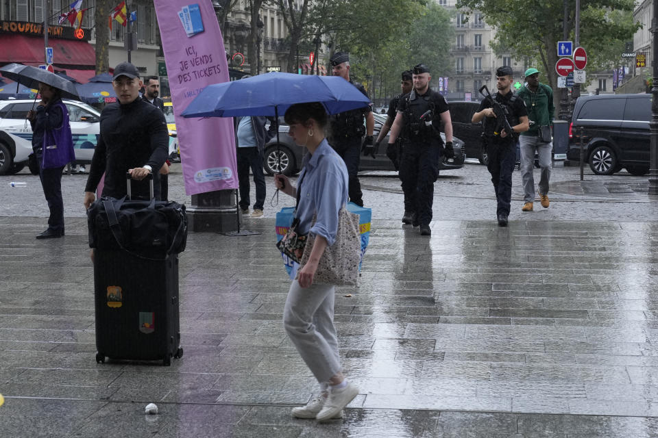 Personas caminan en la calle bajo la lluvia frente a la estación Gare du Nord con los elementos de seguridad de fondo antes del inicio de los Juegos Olímpicos 2024 el viernes 26 de julio del 2024. (AP Foto/Mark Baker)