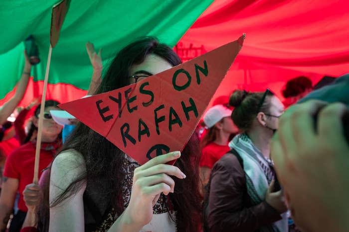 People at a protest holding a red triangular sign reading "Eyes on Rafah."