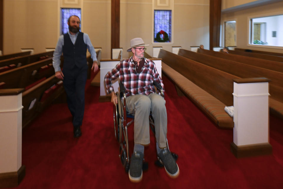 Jerry Lamb, who suffers from a spine condition, talks to Pastor Adam Kelchner at Camden First United Methodist Church Thursday, Dec. 8, 2022, in Camden, Tenn. The church at the urging of the pastor recently had a couple pews cut in half so Jerry, and anyone else who uses a wheelchair, walker or other aid, can still sit with the rest of the congregation. (AP Photo/John Amis)