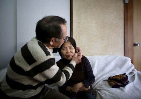72-year-old Kanemasa Ito (L) puts a GPS tracking necklace on his 68-year-old wife Kimiko who was diagnosed with dementia 11 years ago, on a sofa at their home in Kawasaki, south of Tokyo, Japan, April 6, 2016. REUTERS/Issei Kato