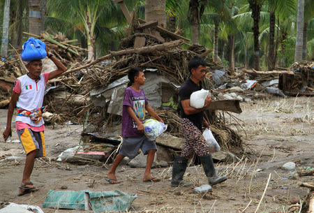 Residents carry relief goods past debris in a village devastated by flash floods in Salvador, Lanao del Norte in southern Philippines, December 24, 2017. REUTERS/Richel V. Umel