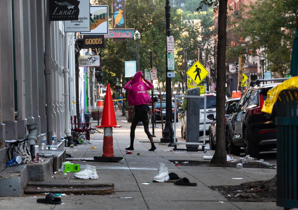 A woman looks for her shoes that were left on Main Street at 13th in Over-the-Rhine, Sunday, August 7, 2022. Overnight, there was a mass shooting leaving nine people injured. The shooting started at Mr. Pitiful's.