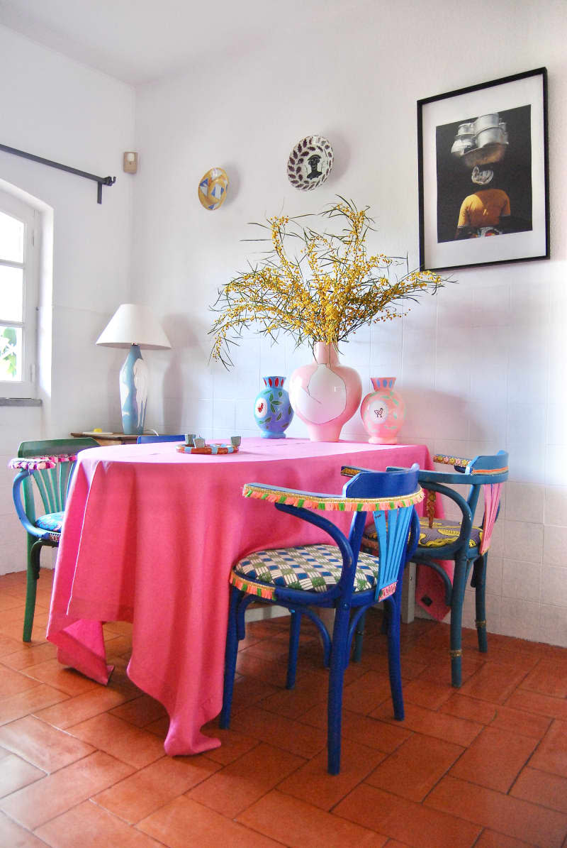 Colorful chairs at table with pink tablecloth in dining area with white walls.