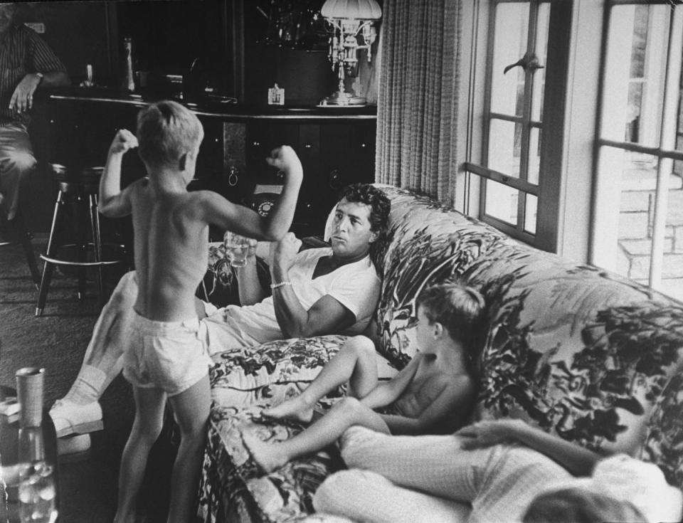 <p>Dean Martin's son flexes his muscles while the singer relaxes with his family at home in 1958. </p>