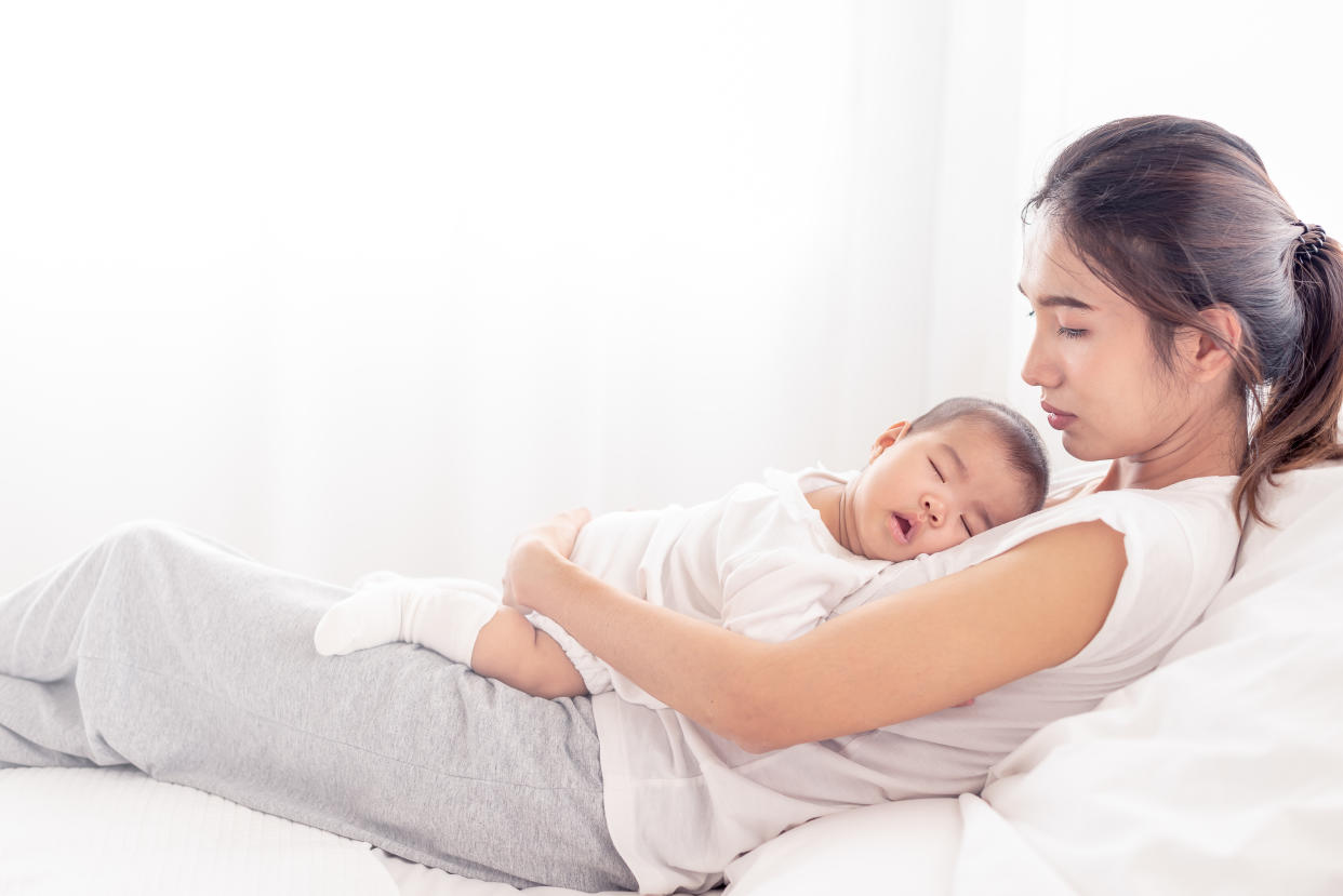 Being mom is so exhausted.  Tired mother laid in bed with newborn baby at night. Authentic real life exhausted parent taking rest with newborn child.