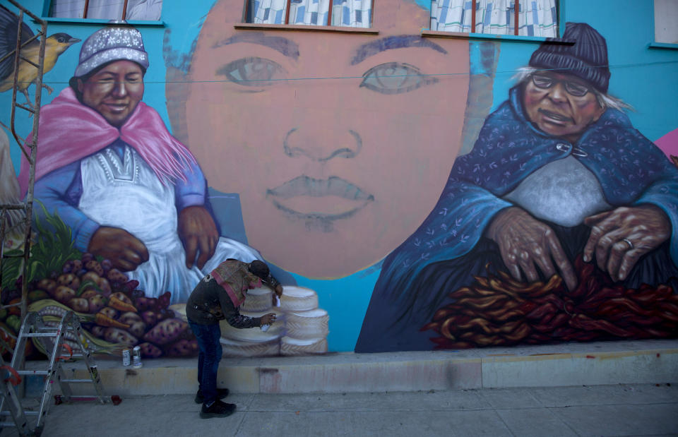 In this May 31, 2019 photo, an urban artist paints a mural featuring an Aymara woman vendor in the Chualluma neighborhood, in La Paz, Bolivia. The state-sponsored project aims to use urban art to capture some of the rich traditions of Bolivia's indigenous culture and turn the area into a tourist attraction. (AP Photo/Juan Karita)