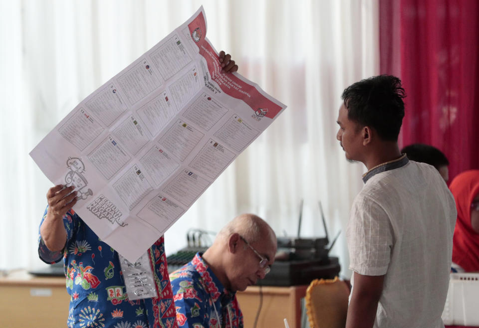 An electoral worker shows a legislative ballot to a voter during the election at a polling station in Jakarta, Indonesia, Wednesday, April 17, 2019. Voting is underway in Indonesia's presidential and legislative elections after a campaign that that pitted the moderate incumbent against an ultra-nationalist former general. (AP Photo/Dita Alangkara)