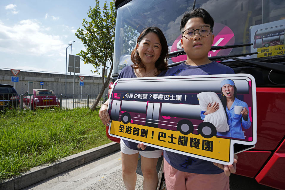 Passengers pose for a photo in front of a double decker bus they got on board, in Hong Kong, Saturday, Oct. 16, 2021. The 76-kilometer (47-mile), five-hour ride on a regular double-decker bus around the territory is meant to appeal to people who are easily lulled asleep by long rides. It was inspired by the tendency of tired commuters to fall asleep on public transit. The banner in orange line reads: 