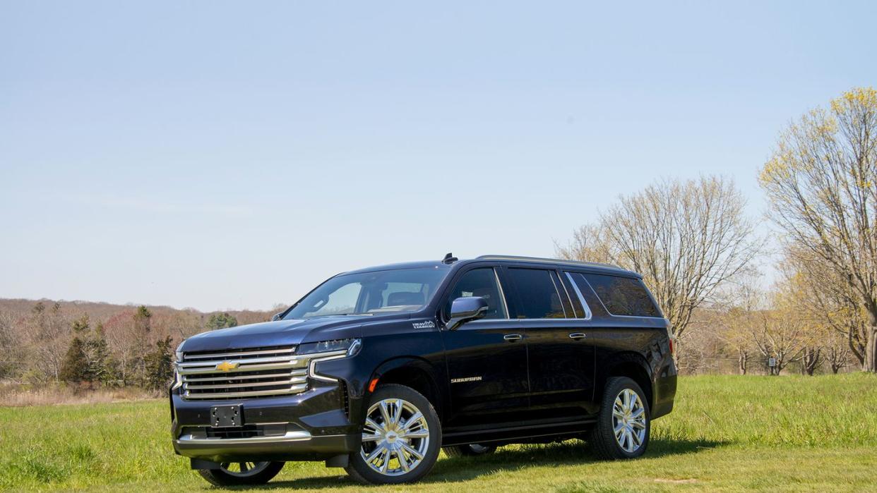 a dark blue four door chevy suburban suv is parked in a field facing the camera