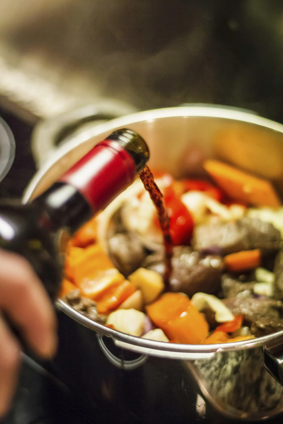 Pouring wine into a pot of beef stew.