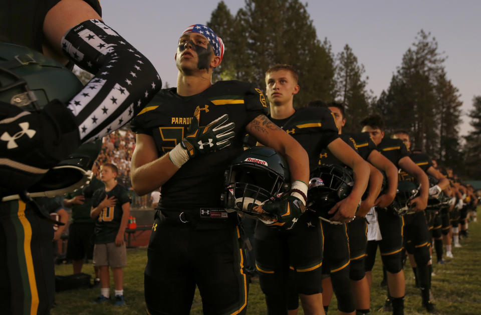 FILE - In this Aug. 23, 2019 file photo, members of the Paradise High School football team stand for the playing of the national anthem before their game against Williams High School in Paradise, Calif. Paradise, the Northern California high school football team is preparing to play for a championship one year after most of the players and coaches lost their homes to a wildfire that nearly destroyed their town. Paradise High School will face Sutter Union High School on Saturday, Nov. 30 for the Northern Section Division III championship.(AP Photo/Rich Pedroncelli, File)